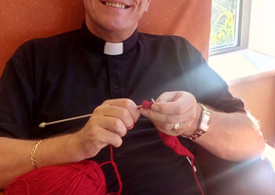 Father John knitting poppies for St Peter and St Paul Church in Borden