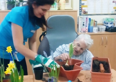 Staff member and resident planting bulbs into painters inside at a table
