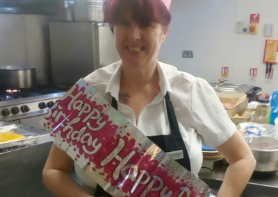 Dining Assistant Paula at Hengist Field Care Home wearing a "Happy Birthday" banner