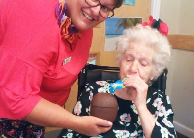 A staff member holding a tropical cocktail for a resident to drink at Hengist Field Care Home